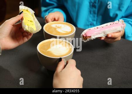 Young women with coffee and eclairs spending time together in cafe, closeup Stock Photo