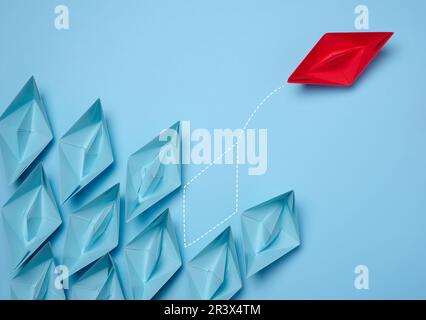 A group of blue paper boats and one red one moving in the opposite direction, the concept of independent personality and breakin Stock Photo