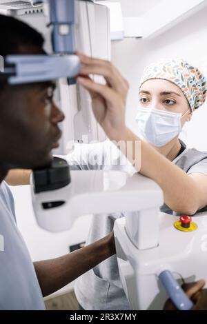 African-American man sitting at an x-ray machine in a dentist's office attended by a specialist Stock Photo