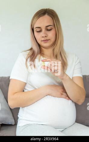 Pregnant woman drinks omega three. Selective focus. White. Stock Photo