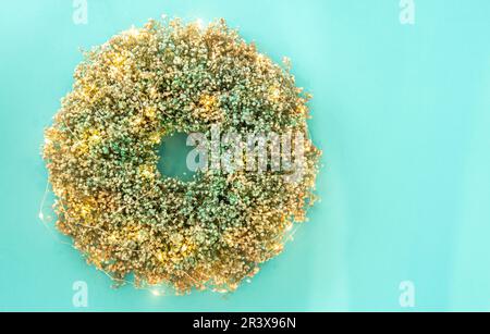 Wreath made of natural flowers with garland lights on blue background, flat lay Stock Photo