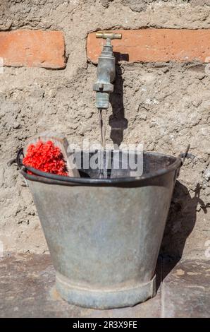 Faucet filling from a metal bucket with a scrubbing brush. Selective focus on water jet Stock Photo