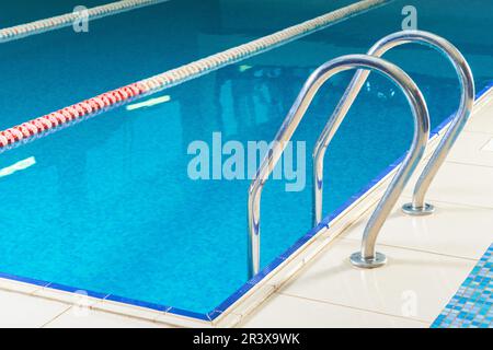 Empty indoor swimming pool with railing and steps in water Stock Photo