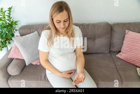 Pregnant woman drinks omega three. Selective focus. White. Stock Photo