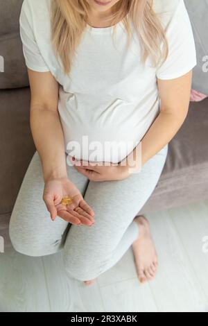 Pregnant woman drinks omega three. Selective focus. White. Stock Photo