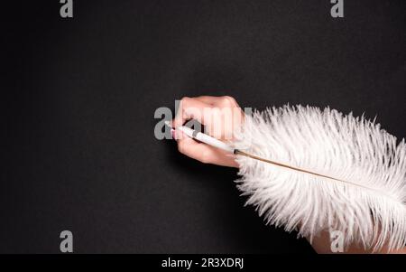 Female hand holding feather pen over black surface Stock Photo