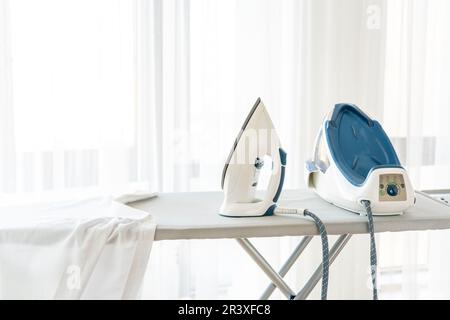 Steam iron standing on ironing board near window with copy space Stock Photo