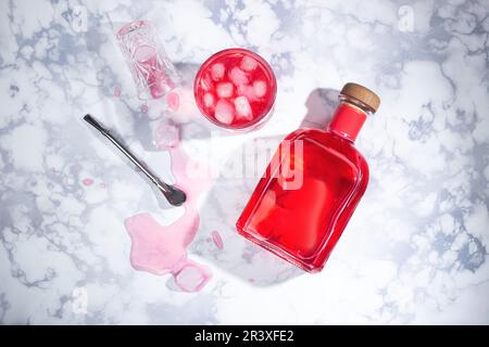 A bottle of red alcohol, a cocktail with liquor and ice next to it in a glass.  The glass fell and the drink spilled, a reusable steel tube.  On a mar Stock Photo