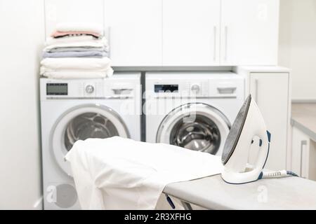 Iron on ironing board with white shirt in laundry room Stock Photo