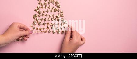 Flat lay of hands making golden christmas tree with star on pink paper Stock Photo