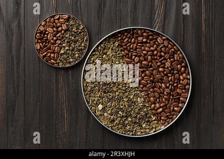 Green dry tea and roasted coffee beans in two round plates of different sizes on a dark wooden background top view copy space. Stock Photo