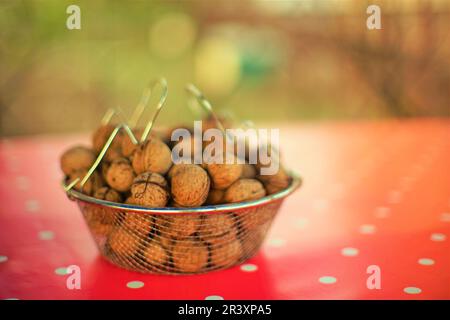 Mesh bowl full of walnuts on a red tablecloth with white dots. Stock Photo