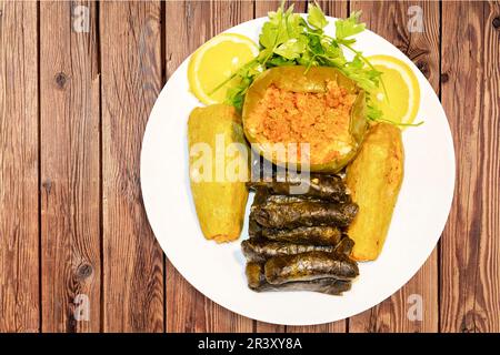 stuffed grape leaves, zucchini, and pepper, with rice and meat served on a white plate with lemon and parsley. Stock Photo