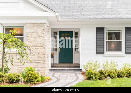 A detail of a front door on home with stone and white bricking siding, beautiful landscaping, and a colorful blue - green front door. Stock Photo