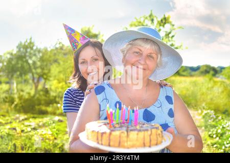 Grandmother's birthday, who with a smile, together with her daughter in the village and holds a birthday homemade cake. Stock Photo