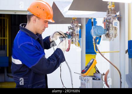 Instrumentation and control engineer diagnoses the operation of gas distribution station equipment on a summer day. A professional worker in a hard hat and overalls diagnoses gas equipment sensors using a multimeter. Authentic worker portrait Stock Photo