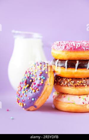 Stack of assorted donuts and a jug of milk on a lilac background. Stock Photo