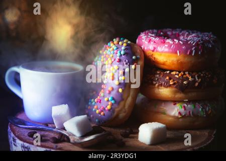 Stack of assorted donuts and a cup of coffee on a dark background. Stock Photo