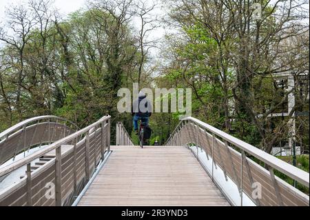 Auderghem, Brussels Capital Region, Belgium - April 29, 2023 - Cyclist driving a bowed wooden bridge at the Brusels high line Stock Photo