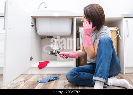 Woman sitting near leaking sink sking for help by phone Stock Photo