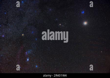 Partial eclipse of the moon below the Pleiades star cluster, and with Orion at left. Stock Photo