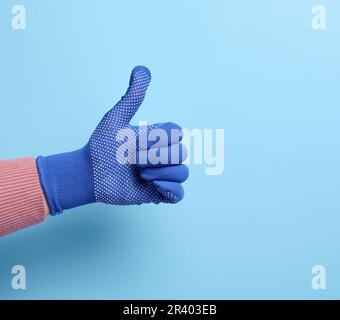 Female hand in blue work protective glove shows the gesture like on a blue background Stock Photo