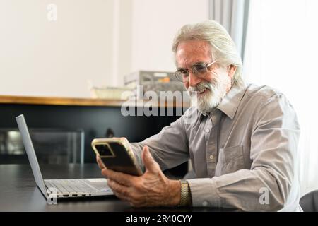 Senior grandfather using laptop and smart phone at home Stock Photo