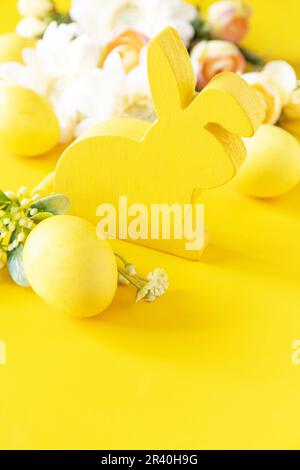 Easter composition with colorful eggs, wooden bunny and spring flowers on yellow background. Copy space. Stock Photo