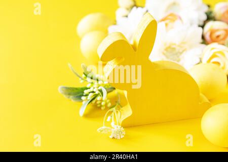 Easter composition with colorful eggs, wooden bunny and spring flowers on yellow background. Copy space. Stock Photo