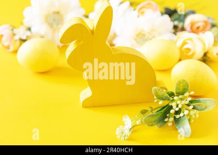 Easter composition with colorful eggs, wooden bunny and spring flowers on yellow background. Copy space. Stock Photo
