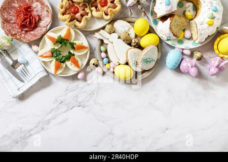 Festive dinner, Easter brunch. Easter table scene with an assortment of baking, desserts, stuffed eggs and dyed eggs on a marble Stock Photo