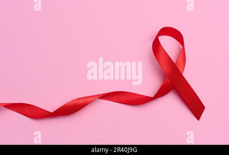 A silk red ribbon in the form of a bow on a pink background, a symbol of the fight against AIDS and a sign of solidarity and sup Stock Photo