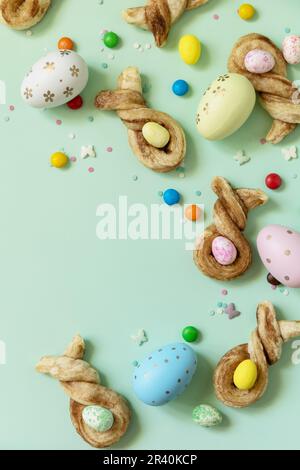 Happy Easter Holidays. Colors Easter eggs with Easter rabbit-shaped buns puff pastry with cinnamon on pastel green background. V Stock Photo