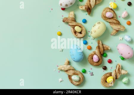 Happy Easter Holidays. Colors Easter eggs with Easter rabbit-shaped buns puff pastry with cinnamon on pastel green background. V Stock Photo