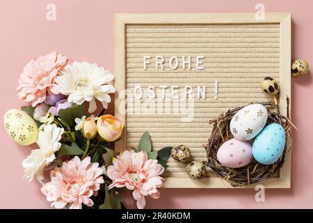 Frohe Ostern - Happy Easter in german greeting, Easter eggs and spring flowers on a pastel pink background, minimalism style com Stock Photo