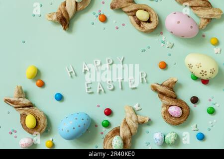 Happy Easter Holidays. Colors Easter eggs with Easter rabbit-shaped buns puff pastry with cinnamon on pastel green background. V Stock Photo