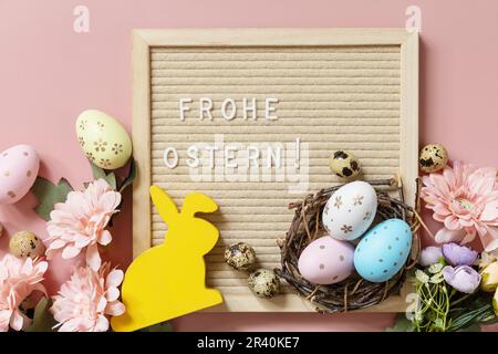 Frohe Ostern - Happy Easter in german greeting, Easter eggs and spring flowers on a pastel pink background, minimalism style com Stock Photo