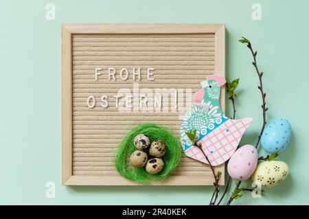 Letter Board with Frohe Ostern - Happy Easter in german greeting, Easter eggs and green branches on a green background. View fro Stock Photo