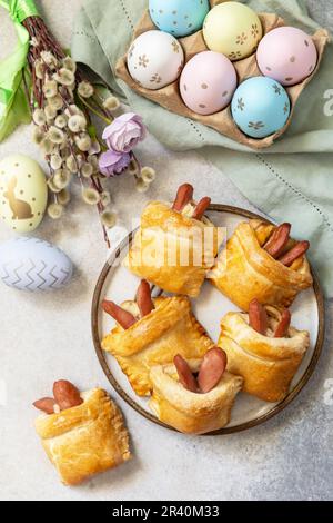 Traditional Easter symbols and food. Buns in the form of an Easter rabbit from sausage and cheese in a yeast dough with colored Stock Photo