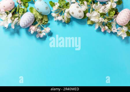 Easter composition with colorful eggs and flowers of apple tree on a blue background.  Spring concept, flowers composition. Gree Stock Photo