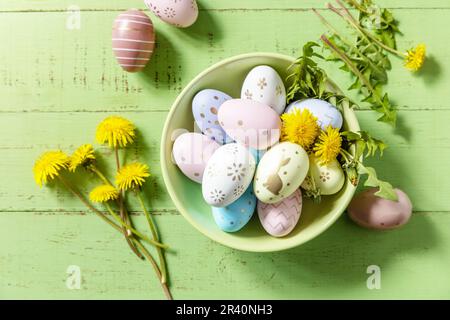 Happy Easter Holidays. Handmade Easter colorful eggs and spring flowers dandelions on a rustic wooden table. Easter composition. Stock Photo