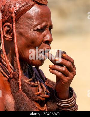 Portrait of an old woman of the Himba tribe with a smoking pipe in her mouth. Stock Photo