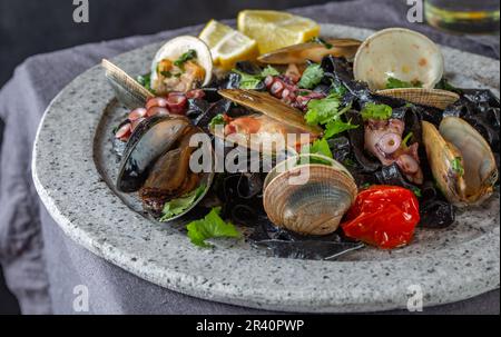 Seafood black fettuccine fehttuchini. Black pasta with squids, octopus clams, mussels on stone plate. Gourmet dish Stock Photo