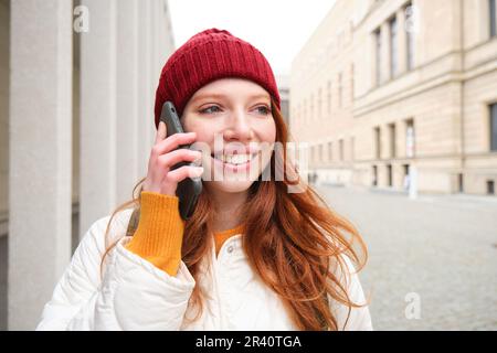 Happy redhead woman, girl with phone talks, has conversation on mobile app, uses internet to call abroad with smartphone app, la Stock Photo