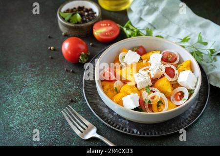 The concept of vegan or diet food. Tomato salad made from a mix of red and yellow tomatoes and feta cheese on a stone tabletop. Stock Photo