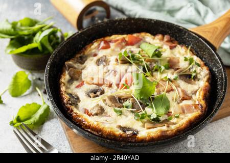 Italian breakfast dish. Rustic omelette (frittata) with mushrooms and bacon on a cast iron pan. Stock Photo