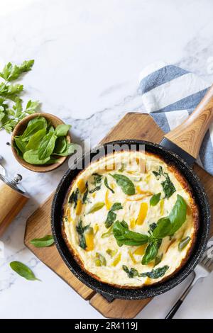Spinach and cheese omelette. Frittata made of eggs, paprika and spinach in a frying pan on a marble countertop. View from above. Stock Photo