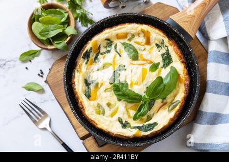 Spinach and cheese omelette. Frittata made of eggs, paprika and spinach in a frying pan on a marble countertop. Stock Photo
