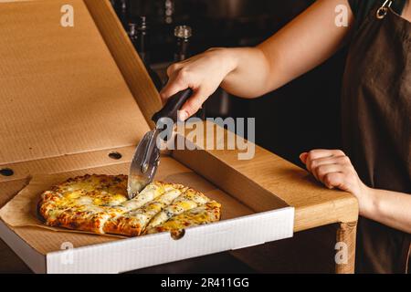 Woman's hand cuts pizza in box with roller knife. Roman square pizza or Pinsa on thick dough, Italian Cuisine Stock Photo