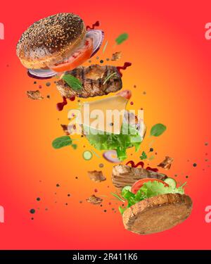 Delicious burger with flying ingredients, pieces of vegetables, spices and meat fried steak on orange background Stock Photo